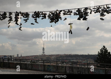 Alten Stiefel hängen an der elektrischen Kabel in Letná Park (letenské Sady) in Prag, Tschechische Republik. Das Panorama von Prag mit dem Fernsehturm Žižkov (Žižkovský vysílač) ist im Hintergrund zu sehen. Entsprechend lokaler Legende, Jugendliche werfen Schuhe auf dem Kabel, wenn sie ihre Jungfräulichkeit verlieren. Stockfoto