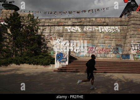 Athleten vorbei durch die Basis des ehemaligen Stalin Monument bedeckt mit Graffiti in Letná Park (letenské Sady) in Prag, Tschechische Republik. Alten Stiefel hängt an der elektrischen Kabel im Hintergrund. Entsprechend lokaler Legende, Jugendliche werfen Schuhe auf dem Kabel, wenn sie ihre Jungfräulichkeit verlieren. Stockfoto