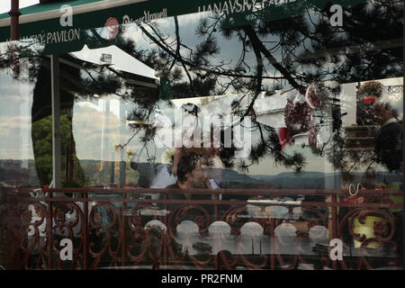 Die Menschen in der Hanavský Pavilon Restaurant in Letná Park (letenské Sady) in Prag, Tschechische Republik, dargestellt durch die Reflexion einer Kiefer und Brücken über die Moldau im Restaurant Fenster. Stockfoto