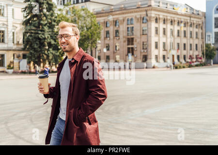 Schöner Mann im Herbst Outfit gehen mit Einweg Kaffeetasse in der Stadt Stockfoto