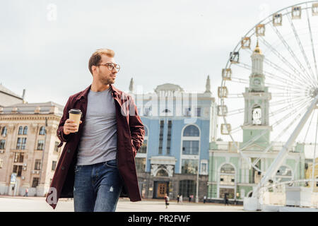 Schöner Mann im Herbst Outfit gehen mit Einweg Kaffeetasse in der Nähe Riesenrad Stockfoto