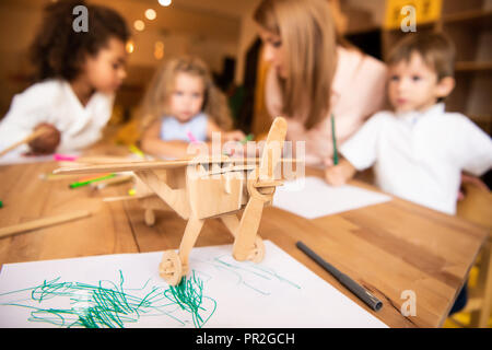 Erzieher und multikulturellen Kinder Zeichnung in Kindergarten, Holz- Ebene im Vordergrund. Stockfoto