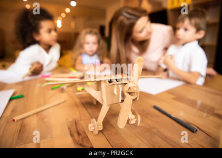 Erzieher und multiethnischen Kinder Zeichnung in Kindergarten, Holz- Ebene im Vordergrund. Stockfoto