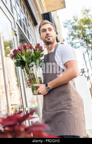 Low Angle View der Florist holding Glas Glas mit Burgund in der Nähe von Roses Flower Shop Stockfoto