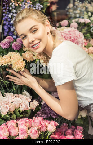 Lächelnd umarmen attraktive florist Blumensträuße in Flower Shop und Suchen an Kamera Stockfoto