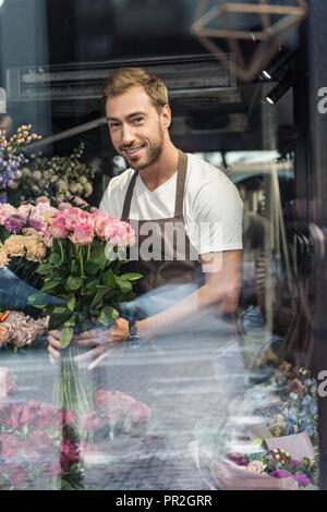 Blick durch die Fenster der stattlichen Florist holding Blumenstrauß aus Rosen in Flower Shop und Suchen an Kamera Stockfoto