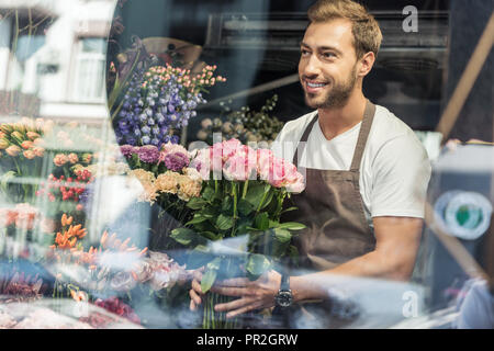 Blick durch die Fenster der stattlichen Florist holding Blumenstrauß aus Rosen im Blumengeschäft und weg schauen Stockfoto