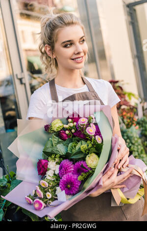 Attraktive florist Holding schönen Blumenstrauß aus Chrysanthemen in der Nähe von Flower Shop und Wegsehen Stockfoto