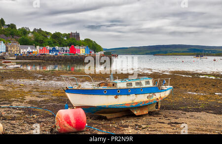 Ein Boot auf dem Boden während der Ebbe in der bunten Stadt von Tobermory auf der Isle of Mull in Schottland mit einer grauen, wolkenverhangenen Himmel gefangen Stockfoto