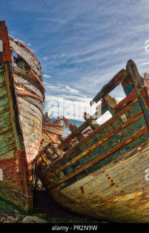 Abstrakte vertikale Foto von zwei grüne und rote hölzerne Boote ruiniert und fällt auseinander, die aus den Elementen unter einem blauen Himmel mit weißen Wolken streifen. Stockfoto