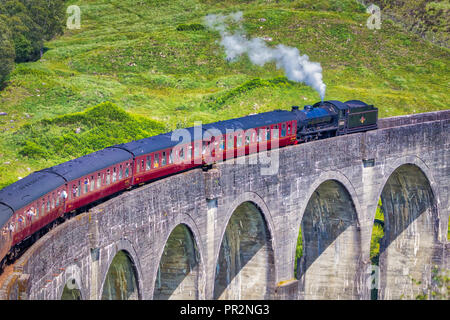 In der Nähe von jacobite Zug über Das Glenfinnan Viaduct reisen mit einem grünen Hügel dahinter und Dampf der Lokomotive Stockfoto