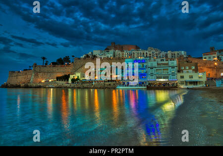 Lange Belichtung von Peniscola und die Burg bei Nacht mit den Lichtern von den Hotels und Restaurants in der Wasser- und dunklen Wolken, die in der tiefen Reflexion Stockfoto