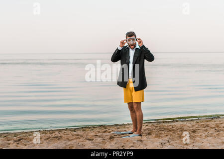 Schockiert, Mann in Schwarz Jacke, Hose und Flossen Maske tragen, Schwimmen am Strand Stockfoto