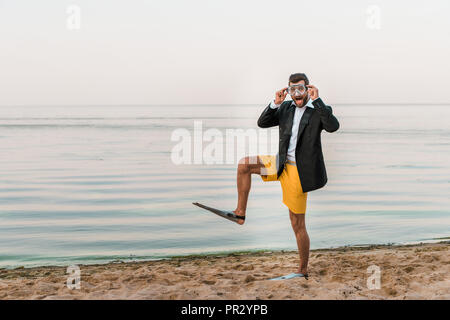 Überrascht Mann in Schwarz Jacke, Hose und Flossen Maske berühren, Schwimmen am Strand in der Nähe von Meer Stockfoto