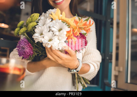 Teilweise mit Blick auf die lächelnde junge Frau mit bunten Strauß aus verschiedenen Blumen im Cafe Stockfoto