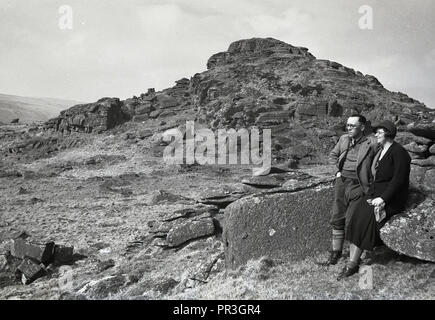 1930er Jahre, historische, ein paar Ruhen im Blick auf Longaford Tor, einem Hügel felsigen Spitze oder Kante an der Dartmoor National Park in Devon, England, Großbritannien, einer natürlichen wilden offenen Moor mit vielen alten Felsformationen oder Granit aufschlüsse als Aufgabenbereiche bekannt. Stockfoto