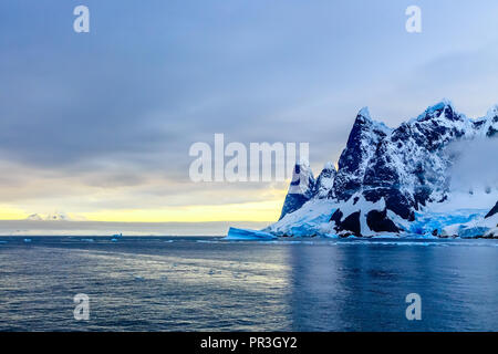 Sonnenuntergang über Klippen, blaue Gletscher und treibenden Eisberg mit Wasseroberfläche im Vordergrund, in der Nähe von argentinischen Inseln, Antarktis Stockfoto