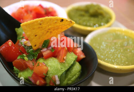 Geschlossen bis Guacamole mit Nachos Chip und verschwommenes Buntes Würzige mexikanische Salsa Soße im Hintergrund Stockfoto