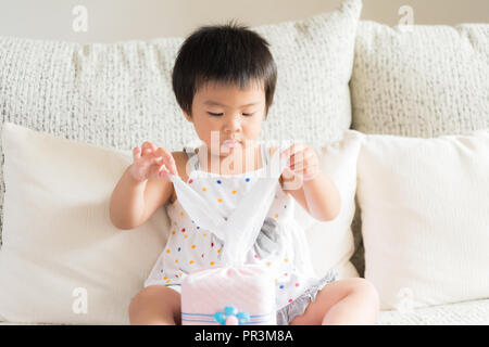 Kranken kleinen asiatischen Mädchen wischen oder Reinigung der Nase mit einem Taschentuch, auf dem Sofa zu Hause sitzen. Medizin und Gesundheit Konzept. Stockfoto