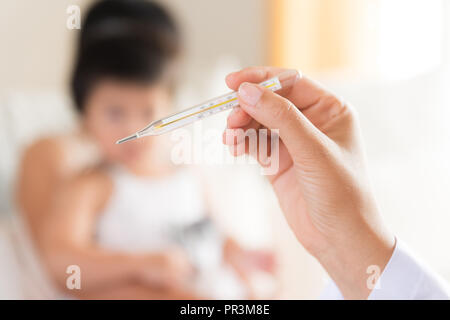 Arzt Holding digitales Thermometer zur Messung der Temperatur von ihren kranken Kind und kranken Mädchen mit Mutter im Hintergrund. Stockfoto