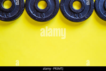 Black Metal Gewichte 1 kg liegen auf einem gelben Hintergrund, flache Ansicht von oben. Stockfoto