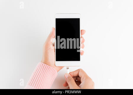 Frau Hände verbinden Ladegerät auf weißem Hintergrund an das Smartphone. Stockfoto