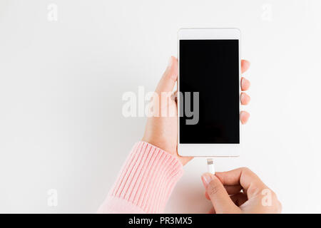 Frau Hände verbinden Ladegerät auf weißem Hintergrund an das Smartphone. Stockfoto