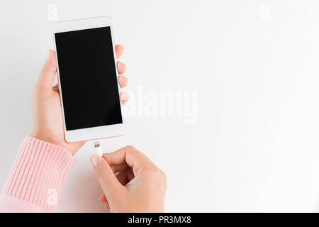 Frau Hände verbinden Ladegerät auf weißem Hintergrund an das Smartphone. Stockfoto