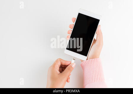 Frau Hände verbinden Ladegerät auf weißem Hintergrund an das Smartphone. Stockfoto