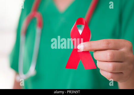 Ärztin mit einem Stethoskop auf die Schulter holding red ribbon HIV, Welt-AIDS-Tag awareness Ribbon. Gesundheitswesen und Medizin Konzept. Stockfoto