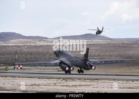 A B-1B Lancer vom 34 Bomber Squadron, Ellsworth Air Force Base, S.D., nimmt als HH-60G Pave Hawk Helikoptern aus der 66th Rescue Squadron im Hintergrund, während Sie im Red Flag 17-3 an der Nellis Air Force Base, Nev Juli 24, 2017 fliegt. Red Flag 17-3 ist in erster Linie auf dem Nevada Test und Training Strecke, die 2,9 Millionen Hektar Land und 5.000 Quadratkilometer von Luftraum von zivilen Luftverkehr über - Flug eingeschränkt durchgeführt. Stockfoto