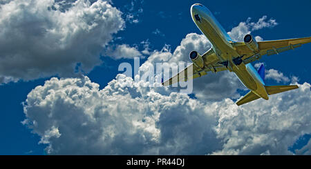 Eine Aktion skyscape Ansicht eines kommerziellen Passagierflugzeugen fliegen closeup in vibrant blue sky, mit entwickelten Weißen cumulonimbus Cloud. Stockfoto