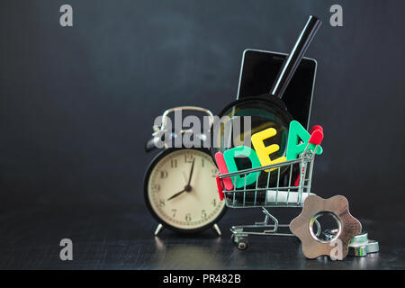 Bunte Buchstaben der Idee mit Uhr, Lupe, Smartphone, Zahnräder in einem Korb auf einem schwarzen Hintergrund Copyspace Stockfoto