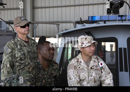 Von links: U.S. Navy Bau Elektriker 1. Klasse Richard Englisch mit Küsten Riverine Squadron 8 (CR8), ugandische Oberstleutnant Nelson Aheebwa mit der Ugandischen People's Defence Force und Japanische Maj. Shinsuke Takada mit der Japan Masse Verteidigung-kraft hören während einer kurzen auf Lager Lemonnier, Dschibuti, Sept. 14, 2018. Beide Aheebwa und Takada, ausländische Verbindungsbeamte aus ihren jeweiligen Ländern Combined Joint Task Force-Horn von Afrika zugeordnet, nahmen an einer kurzen CRS 8 und tourte eine Der patrouillenboote. Stockfoto