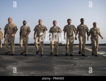 Golf von Aden (Sept. 14, 2018) Chief Petty Officer selectees singen "Anker Weg" während eines Chief Petty Officer pinning Zeremonie auf dem Flugdeck der Whidbey Island-Klasse dock Landung Schiff USS Rushmore (LSD 47), die während einer planmäßigen Einsatz der Essex Amphibious Ready Group (ARG) und 13th Marine Expeditionary Unit (MEU). Das Essex ARG/13 MEU ist tödlich, flexibel, und anhaltende Navy-Marine Corps Team in die USA 5 Flotte Bereich der Maßnahmen zur Unterstützung der Marine im Einsatz für die Stabilität und Sicherheit in der Region zu gewährleisten, die Verbindung mit dem Mittelmeer und Th Stockfoto