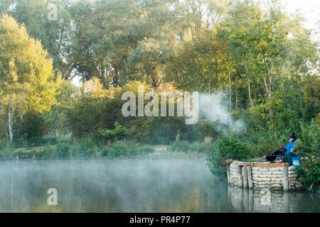 Angler auf einem Karpfen Angelsee mit einem Hauch von Vape in der Luft. Stockfoto