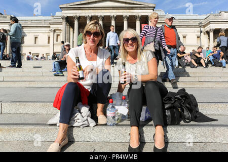 London, Großbritannien. September 2018. Zwei Personen entspannen sich auf den Stufen des Trafalgar Square, London, genießen Getränke in Flaschen und lächeln in die Kamera. Die Nationalgalerie bildet die architektonische Kulisse, während andere in der Nähe sitzen oder spazieren gehen und eine lebhafte und gesellige Atmosphäre in einem der berühmtesten öffentlichen Bereiche der Stadt schaffen. Penelope Barritt/Alamy Live News Stockfoto