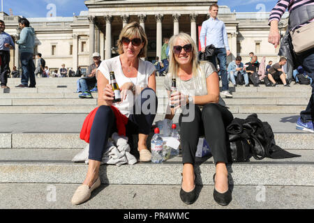 London, Großbritannien. September 2018. Zwei Personen entspannen sich auf den Stufen des Trafalgar Square, London, genießen Getränke in Flaschen und lächeln in die Kamera. Die Nationalgalerie bildet die architektonische Kulisse, während andere in der Nähe sitzen oder spazieren gehen und eine lebhafte und gesellige Atmosphäre in einem der berühmtesten öffentlichen Bereiche der Stadt schaffen. Penelope Barritt/Alamy Live News Stockfoto