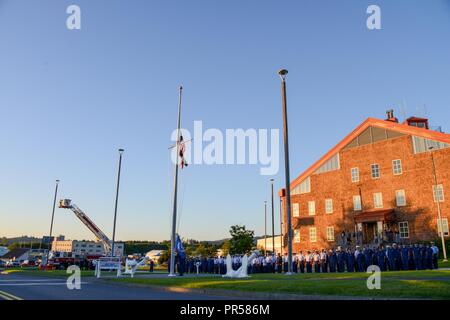 Petty Officer 3rd Class Jordanien Salazar und Petty Officer 3rd Class James Linkenhoker, beide Mitglieder der Base Kodiak's Personal Services Department, der Nationalen Ensign auf Halbmast für 9/11 Gedenkveranstaltung an der Basis Kodiak, Alaska, Sept. 11, 2018. Teilnehmer Zeugnis Zeremonien, bestehend aus einem Gebet mit dem Kaplan und eine Einhaltung der Ereignisse, Sept. 11, 2001. Us-Küstenwache Stockfoto