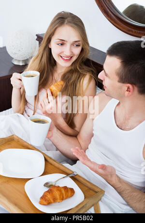 Glückliche Menschen und positive Freundin mit leckeren Frühstück im Bett Stockfoto