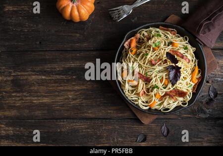 Herbst Pasta mit Kürbis und Speck in gusseisernen Pfanne. Hausgemachte spaghetti Kürbis Pasta auf Holz, kopieren. Herbst saisonale Gerichte. Stockfoto
