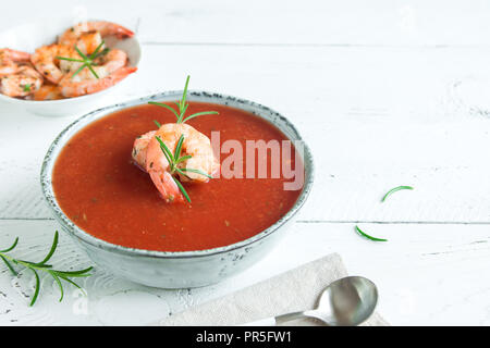 Pflanzliche Tomatensuppe Gazpacho mit Garnelen (Garnelen) und Rosmarin in der Schüssel auf weißem Holz- Hintergrund, Ansicht von oben, kopieren. Stockfoto