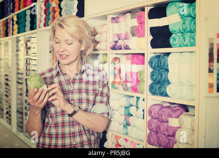 Reife blonde Frau mit bunten Garnen im Nähen departament Store Stockfoto