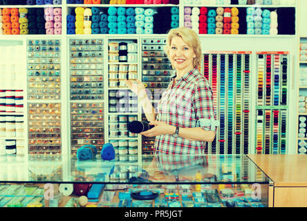 Portrait von Reifen lächelnd weibliche Kassierer an der Kasse mit Stricken wolle im Shop Stockfoto