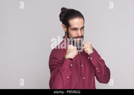 Porträt von Ernst stattlicher Mann mit dunklen gesammelt, lange Haare und Bart im roten Hemd stehend, mit Blick auf die Kamera mit dem Boxen Fäuste und bereit zu Attac Stockfoto