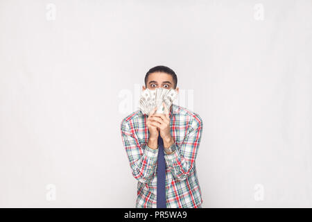 Portrait von Reichen hübscher junger Erwachsener Geschäftsmann in bunt karierten Hemd mit blauer Krawatte stehend und Fan von Dollar mit großen Augen verrückt. Ich Stockfoto