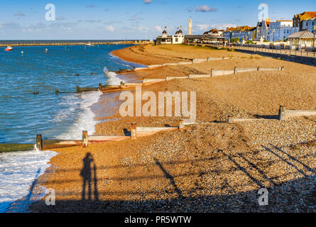 Am späten Nachmittag im Herbst Sonne dreht die Kieselsteine am Strand und Holz- groyne Wasser Leistungsschalter in Herne Bay, Kent, Großbritannien eine goldene Farbe. Der Schatten einer p Stockfoto