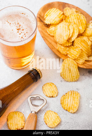 Glas und Flasche Handwerk Lagerbier mit Kartoffelchips Snack und Opener auf Stein Küche Hintergrund. Bier und Imbiss. Stockfoto