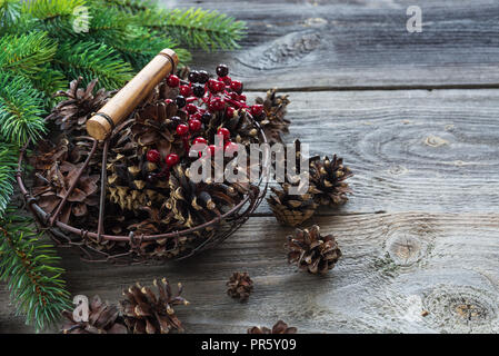 Weihnachten Konzept: volle Korb mit Tannenzapfen und roten Stechpalme Beeren und Zweige auf dem Hintergrund der alten unlackierte Holz Fichte, mit copy-spa Stockfoto