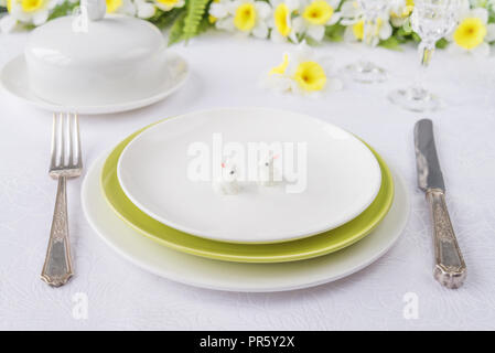 Klassische dienen für eine Ostern Abendessen mit weißem und grünem Porzellan Teller, Besteck und Frühling Blumen auf einem weißen Tischtuch Stockfoto